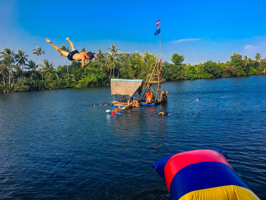 A person jumping into blue water with onlookers in a floating hut
