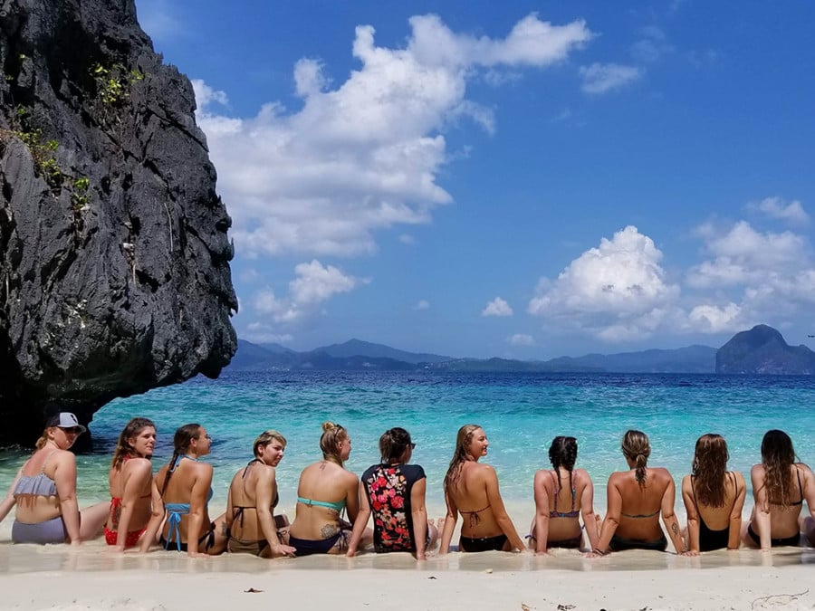 Travellers sitting in a row on a beach with pristine water
