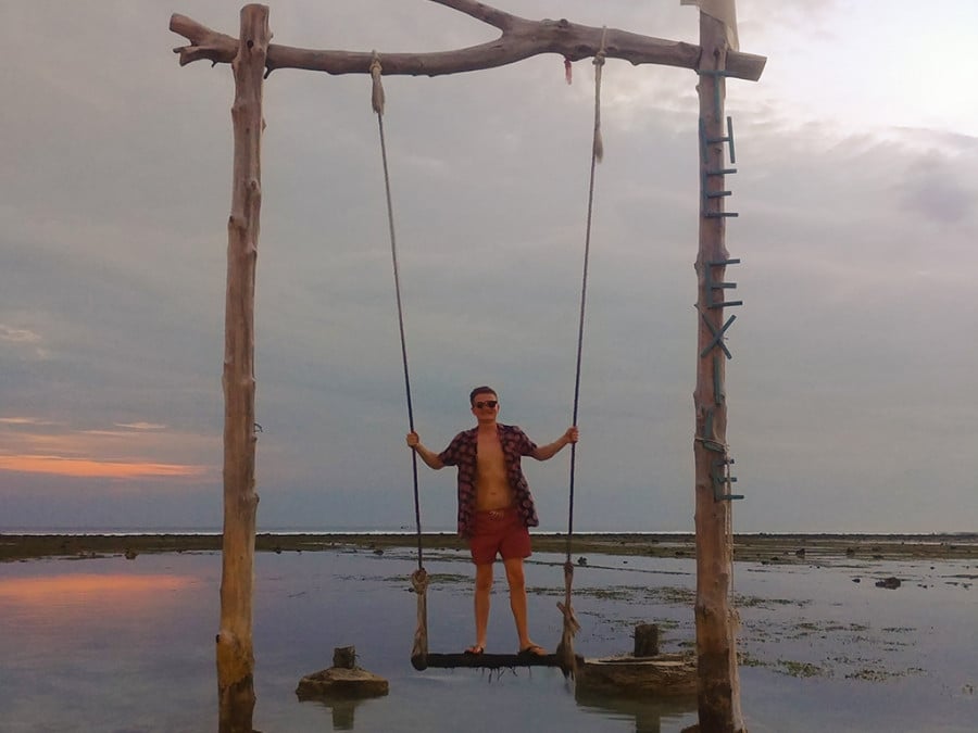 Man on a swing over water at sunset
