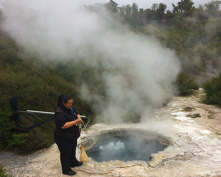 A guide next to a geothermal hot water geyser with rising steam