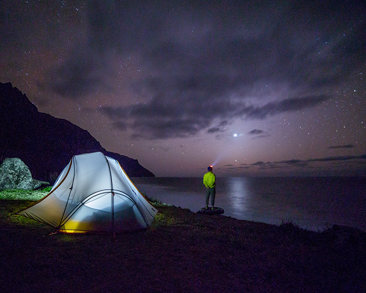 A man next to a tent looking at the night sky
