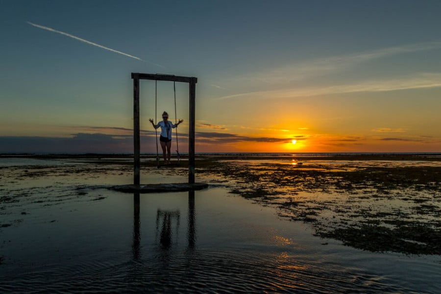Person standing on a swing above water during sunset