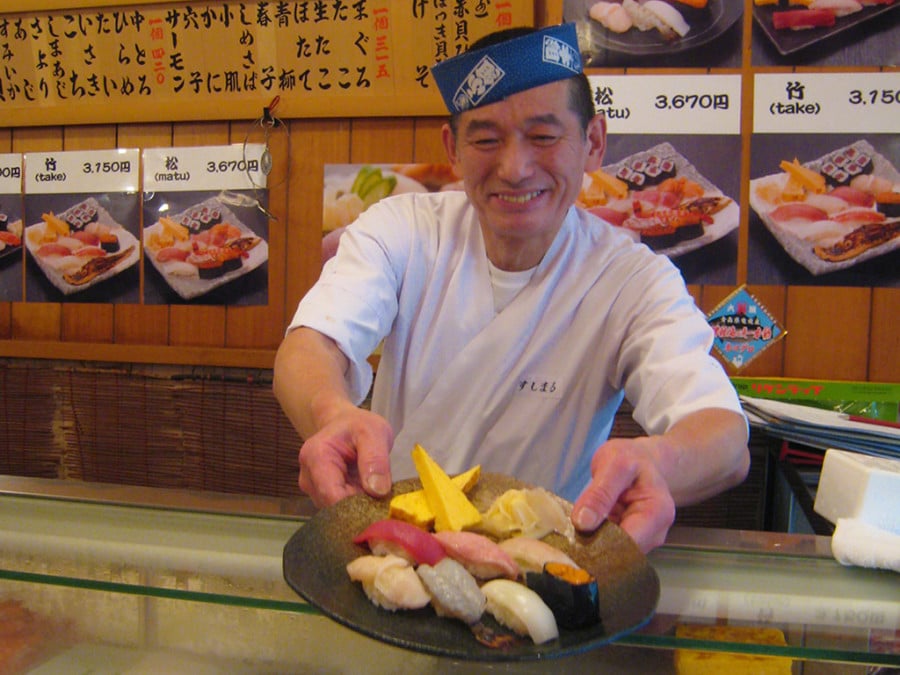 A sushi chef presenting a plate of sushi