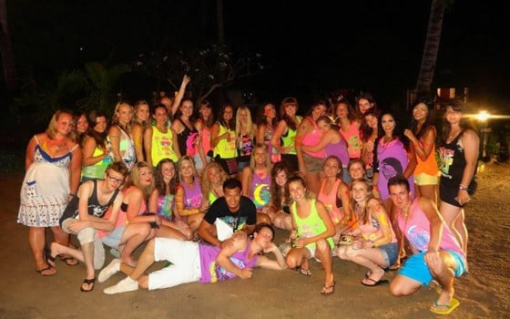 A group of travellers in bright clothing pose for a photo during a full moon party