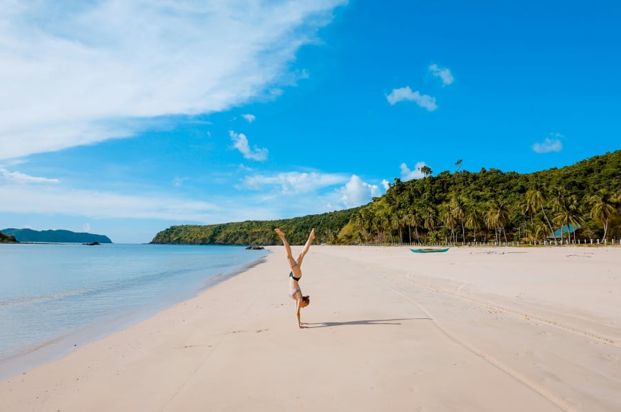 Traveller doing handstand on sandy Palawan beach