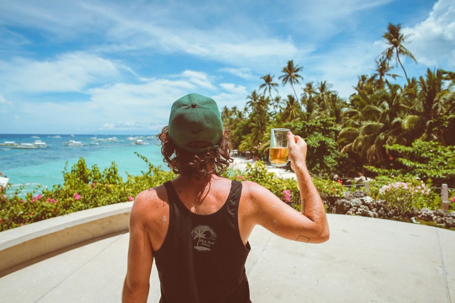 Traveller looking at view of Alona Beach with a beer in hand